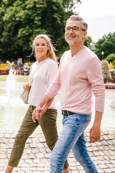 Ein Paar spaziert Hand in Hand an einem Teich mit blühenden Blumen im Hintergrund.