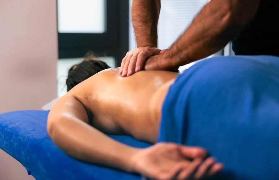 Rückenmassage in einer Praxis Eine Person erhält eine Rückenmassage auf einer blauen Liege, während ein Masseur mit einem Hand auf ihrem Rücken arbeitet.