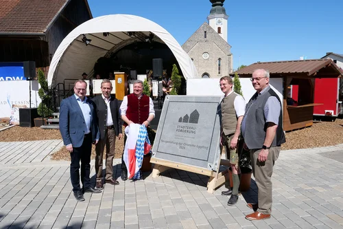 Stadtentwicklung Gedenktafel Enthüllung Fünf Männer stehen lächelnd vor einer Gedenktafel zur Stadtentwicklung. Im Hintergrund sind ein Zelt, eine Bühne und eine Kirche zu sehen.