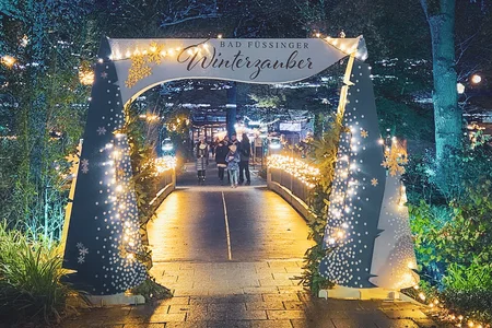 Eingang zum Bad Füssen Winterzauber Ein festlich beleuchteter Eingang zum Winterzauber in Bad Füssen, umgeben von Bäumen mit leuchtenden Blättern und Lichtern.