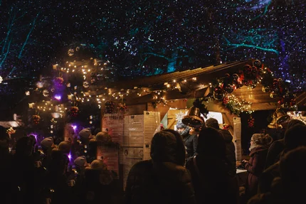 Weihnachtsmarkt bei Nacht Ein festlich geschmückter Stand auf einem Weihnachtsmarkt mit fröhlichen Menschen und vielen Lichtern, die eine gemütliche Atmosphäre schaffen.