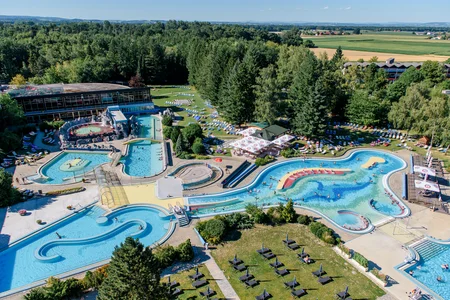 Wasserpark mit Schwimmbädern Ein großer Wasserpark mit mehreren Becken, Rutschen und Liegen. Menschen schwimmen in verschiedenen Bereichen, während im Hintergrund Bäume und Wiesen sichtbar sind.