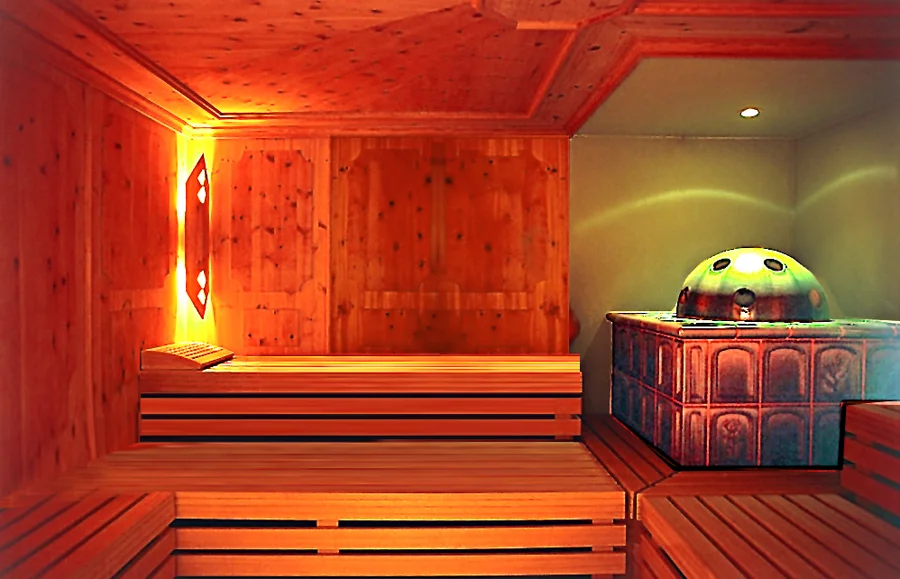 Wooden sauna interior In a wooden sauna, there is a bench made of slats, a small table, and a round heater with a metal top. Soft lighting creates a warm atmosphere. The walls are also wooden with subtle texturing.