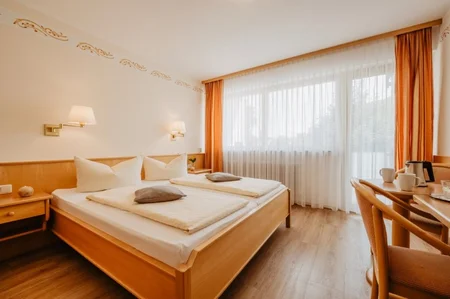 Ein helles Hotelzimmer mit zwei Betten, Kaffeetassen und einer Aussicht auf den Außenbereich durch große Fenster.