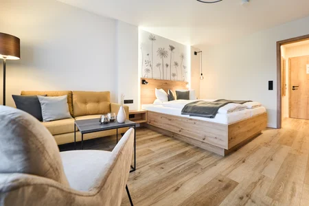 Modernes Hotelzimmer Ein modernes Hotelzimmer mit einem Doppelbett, einem Sofa und einem Tisch. An der Wand sind florale Muster zu sehen. Der Raum hat Holzfußboden und ein warmes Licht.