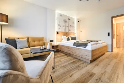 Modernes Hotelzimmer Ein modernes Hotelzimmer mit einem Doppelbett, einem Sofa und einem Tisch. An der Wand sind florale Muster zu sehen. Der Raum hat Holzfußboden und ein warmes Licht.