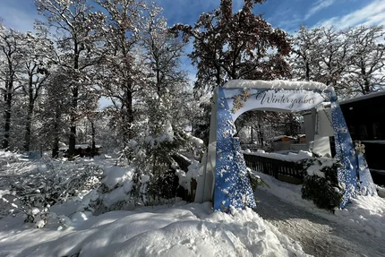 Winter magic entrance A snow-covered landscape with trees and an archway reading 'Winterzauber' in a winter setting.
