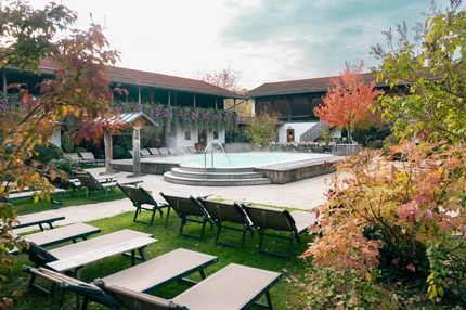 Außenbereich der Therme mit einem dampfenden Becken, Liegestühlen und herbstlich gefärbten Bäumen.