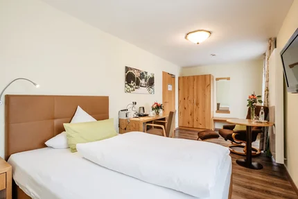 Modernes Hotelzimmer Ein Blick auf ein modernes Hotelzimmer mit einem Bett, Schreibtisch und Stuhl. Eine Holzkommode steht im Raum neben einer Pflanze und einem Bild an der Wand.