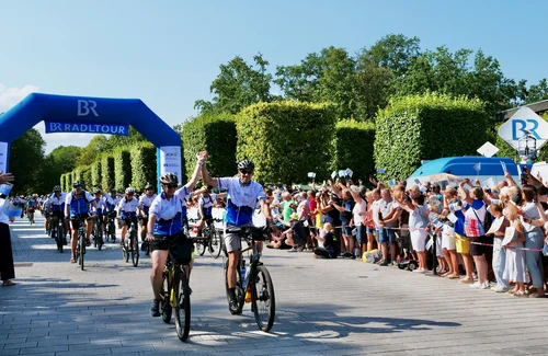 Fahrradveranstaltung mit Feiern Gruppe von Radfahrern, die durch ein Zielbogen fahren, Feiern im Hintergrund.