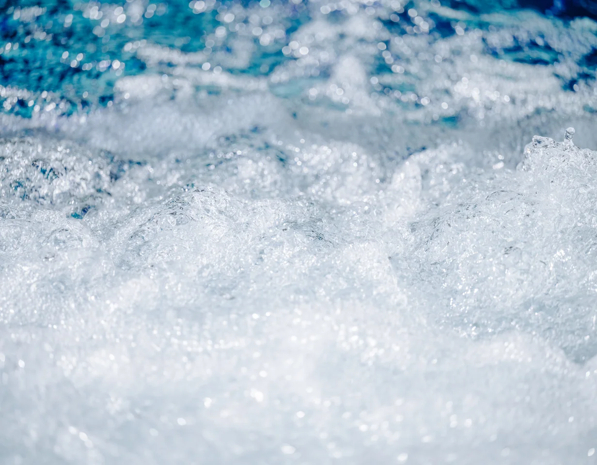 Schäumendes Wasser Nahaufnahme von schäumendem Wasser mit Bläschen und einer blauen Struktur im Hintergrund.
