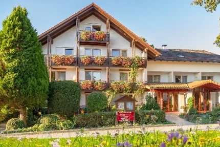 Ein dreigeschossiges Gebäude mit Blumenkästen an den Fenstern und üppiger Grünpflanzendekoration vor der Eingangstür.