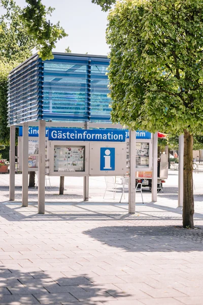 Ein Informationspunkt im Freien mit einem älteren Paar, das auf Stühlen sitzt. Bäume umgeben den Bereich.