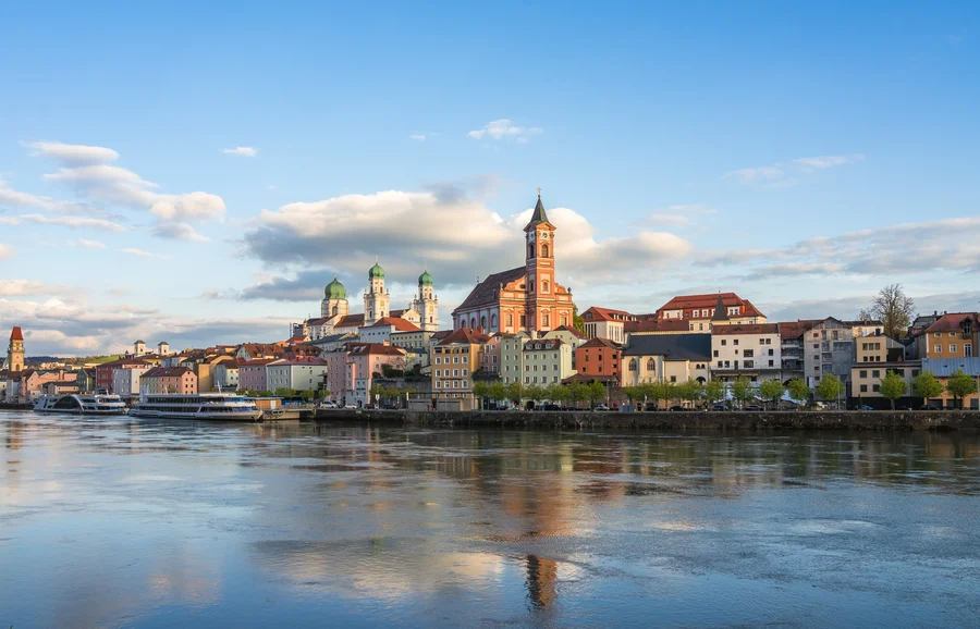 Eine Stadtansicht auf der linken Seite des Gerinnes mit bunten Gebäuden und Kirchen mit grünen Kuppeln im Hintergrund. Der Himmel zeigt einige Wolken und das Licht ist sanft.