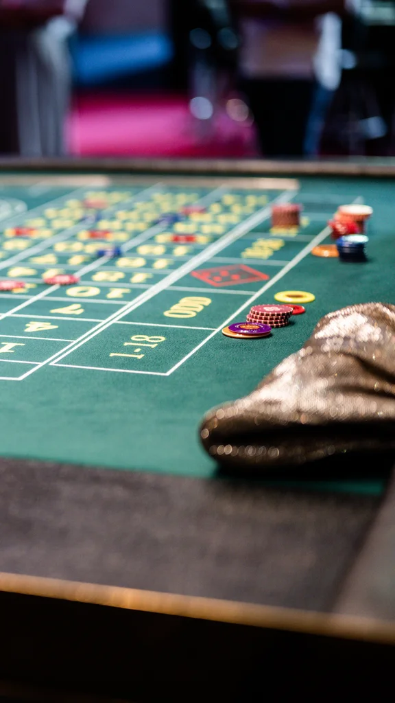 Glücksspieltisch mit Chips Ein Glücksspieltisch mit verdeckten Wetten, darunter Spielchips und eine Hand eines Dealers, die auf den Tisch zeigt.