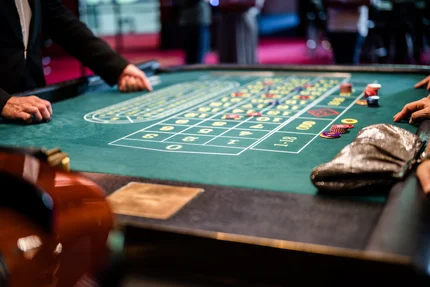 Glücksspieltisch mit Chips Ein Glücksspieltisch mit verdeckten Wetten, darunter Spielchips und eine Hand eines Dealers, die auf den Tisch zeigt.
