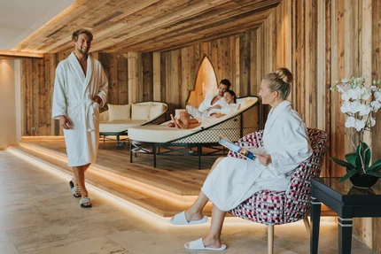 Entspannte spa Szenario Eine entspannende Spa-Umgebung mit Menschen in Bademänteln. Ein Mann geht, während ein Paar auf einer Liege entspannt und eine Frau in einem Sessel ein Magazin liest.