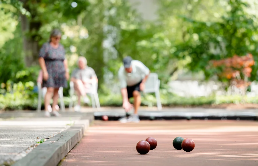Eine Gruppe von Personen spielt Boule im Freien. Auf dem Boden liegen mehrere Boulekugeln, während die Spieler sich auf das Spiel konzentrieren.